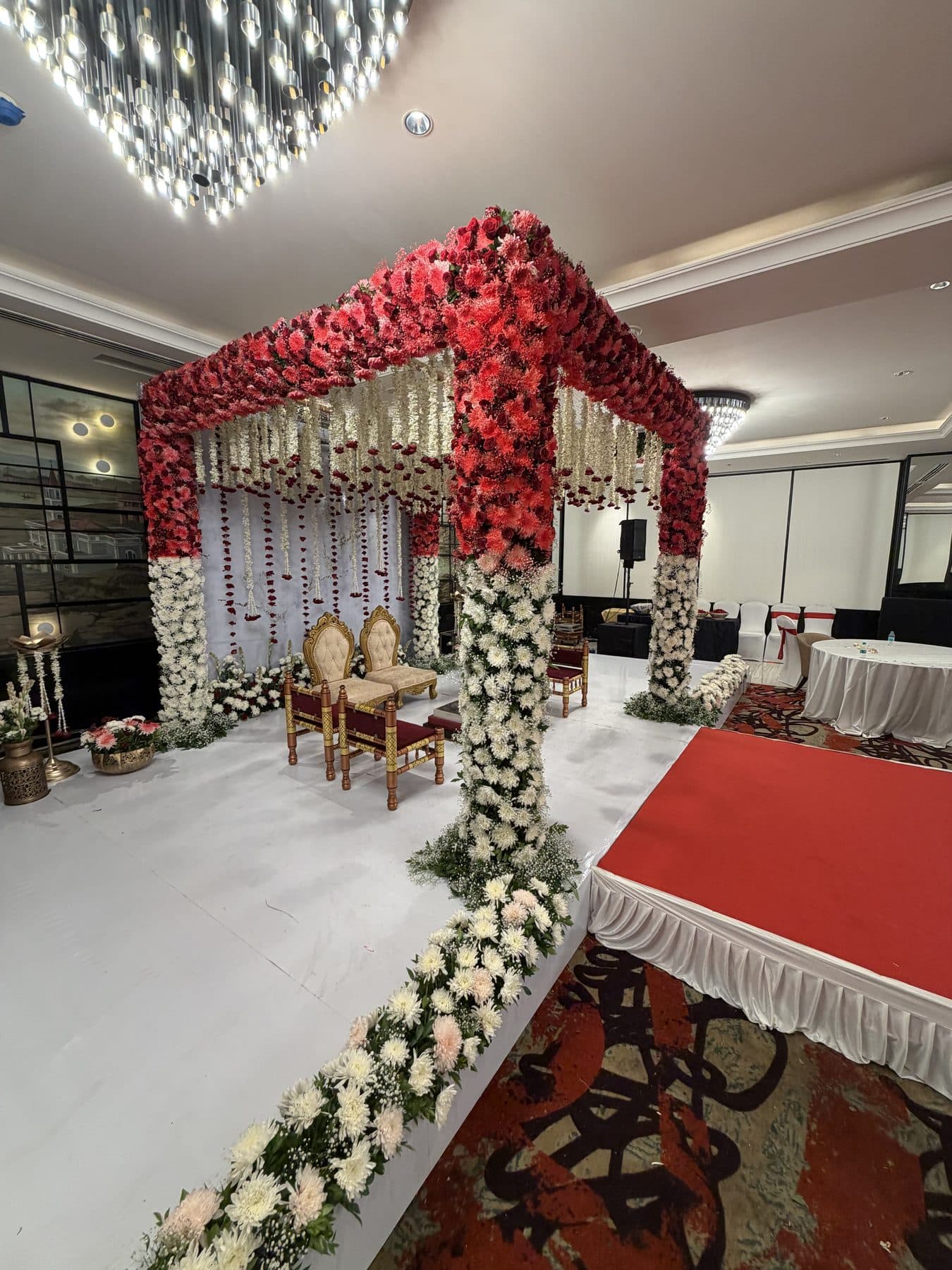 A red and white floral mandap with hanging strand décor built by the FlaminQo décor team